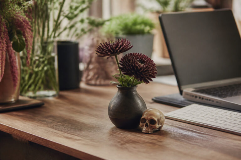 Small bud vase Halloween arrangement with mums on an office desk beside a laptop