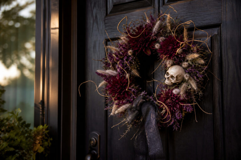 Finished Halloween wreath with dark dahlias, dried statice, and a black ribbon bow hanging on a front door
