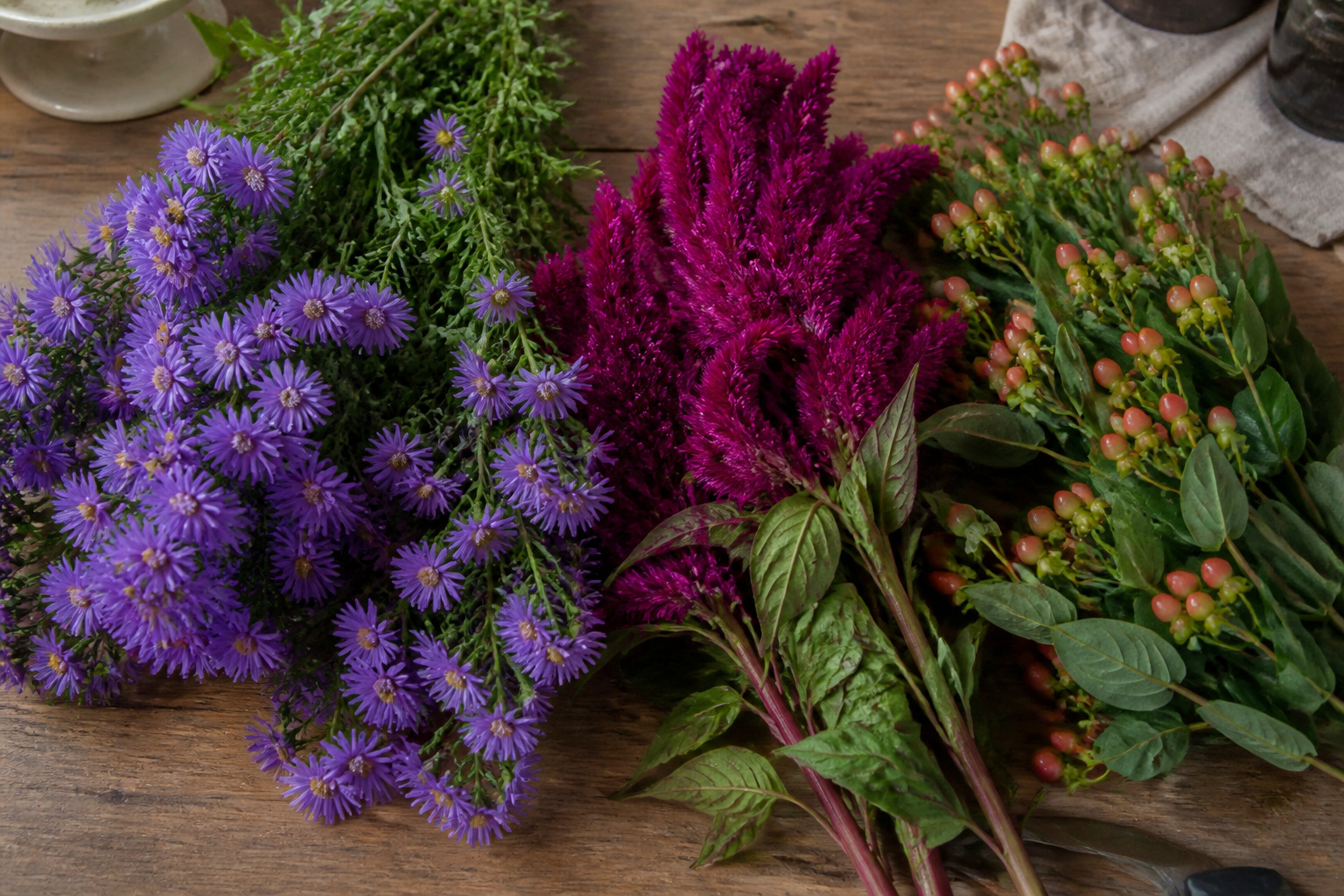 Purple asters, plume celosia, and hypericum berries arranged together on a worktable