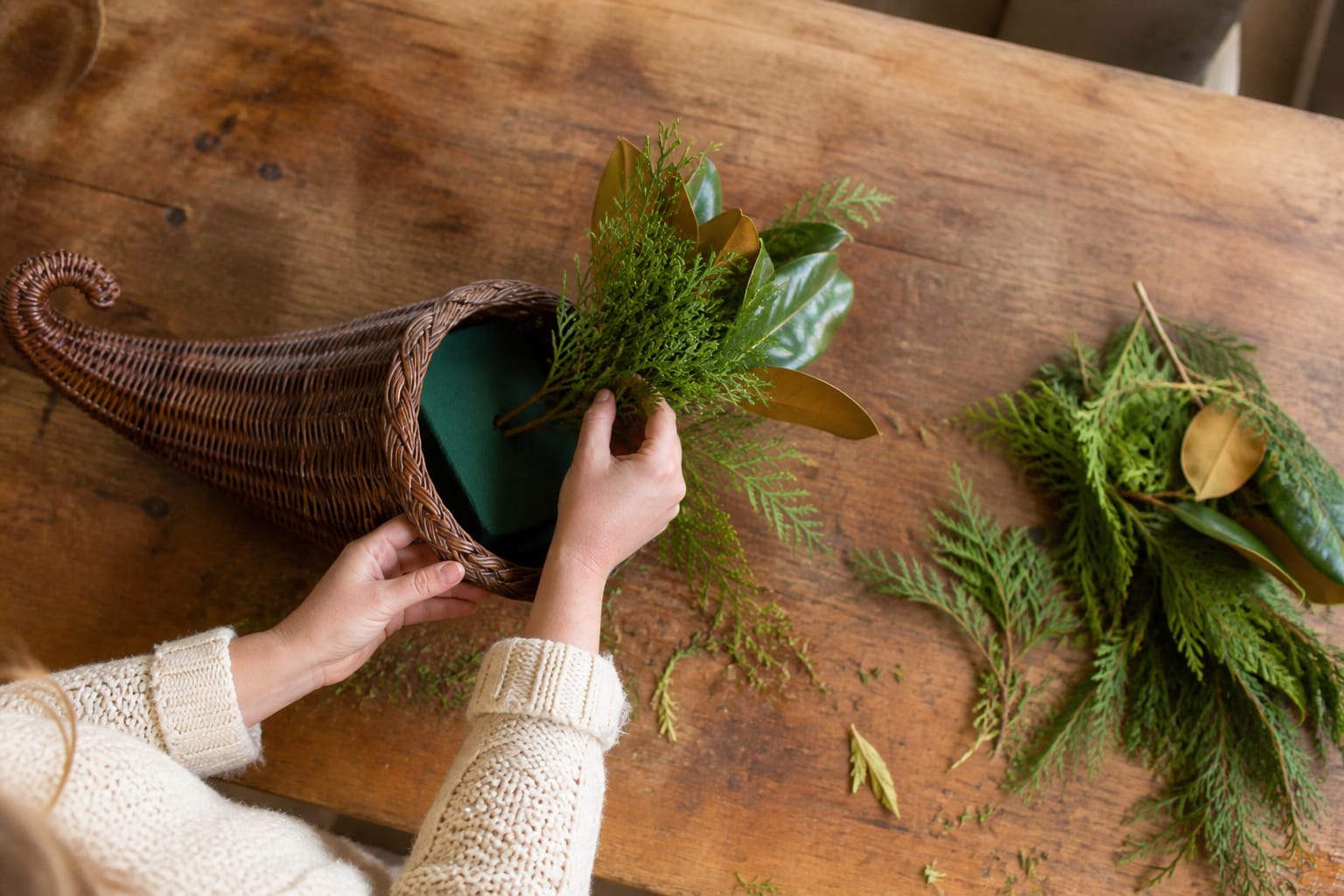Fresh fall greenery being inserted into floral foam inside a cornucopia basket