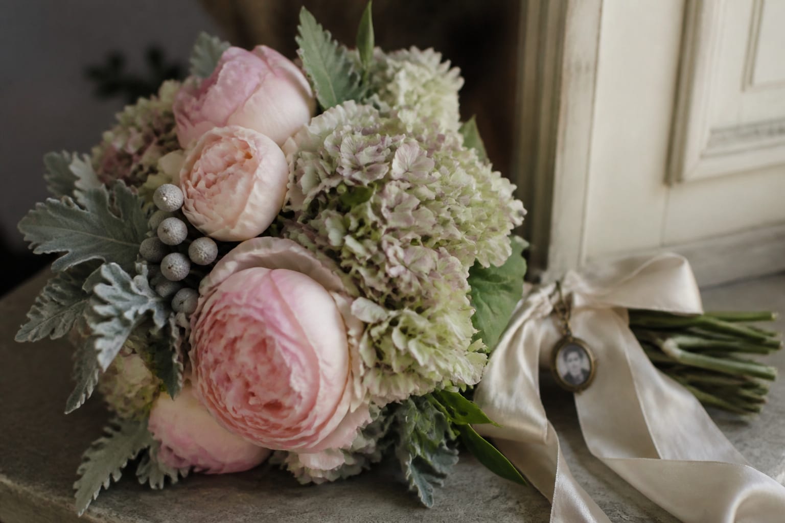 Heritage-style bouquet of blush peonies and muted hydrangea with a vintage locket charm