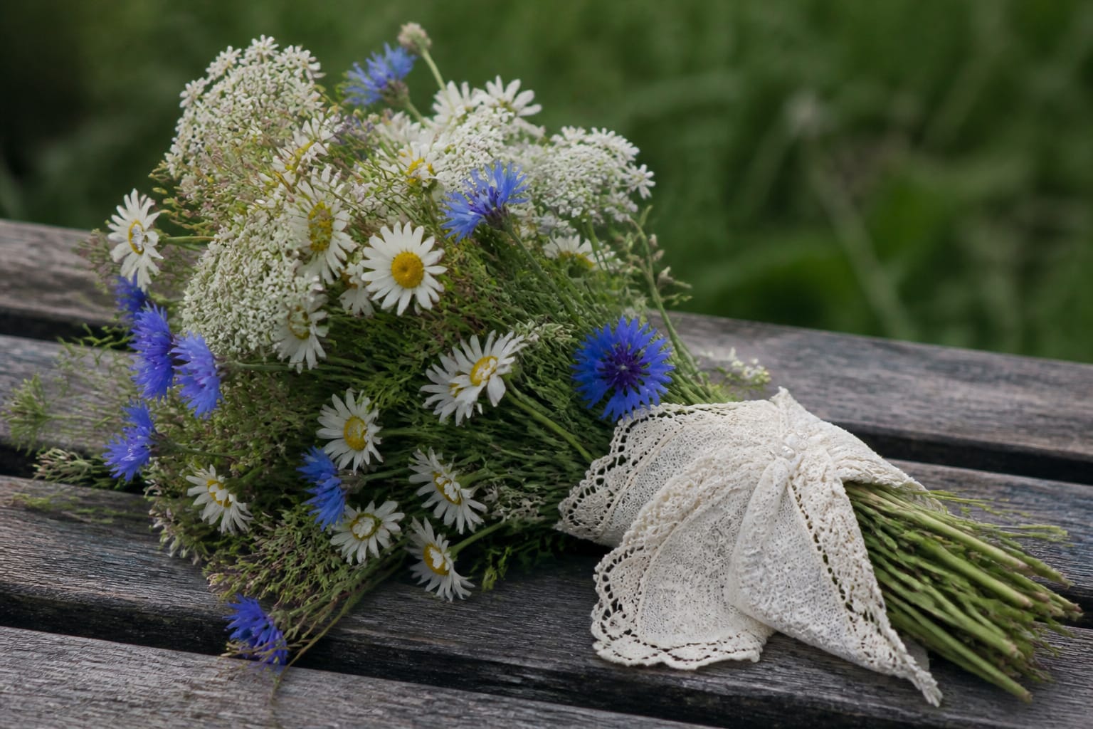 Rustic wildflower bouquet of daisies and cornflowers wrapped in antique lace