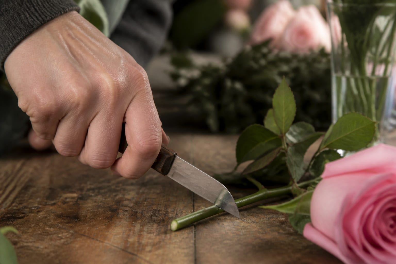 Florist using a straight-blade floral knife to cut a rose stem