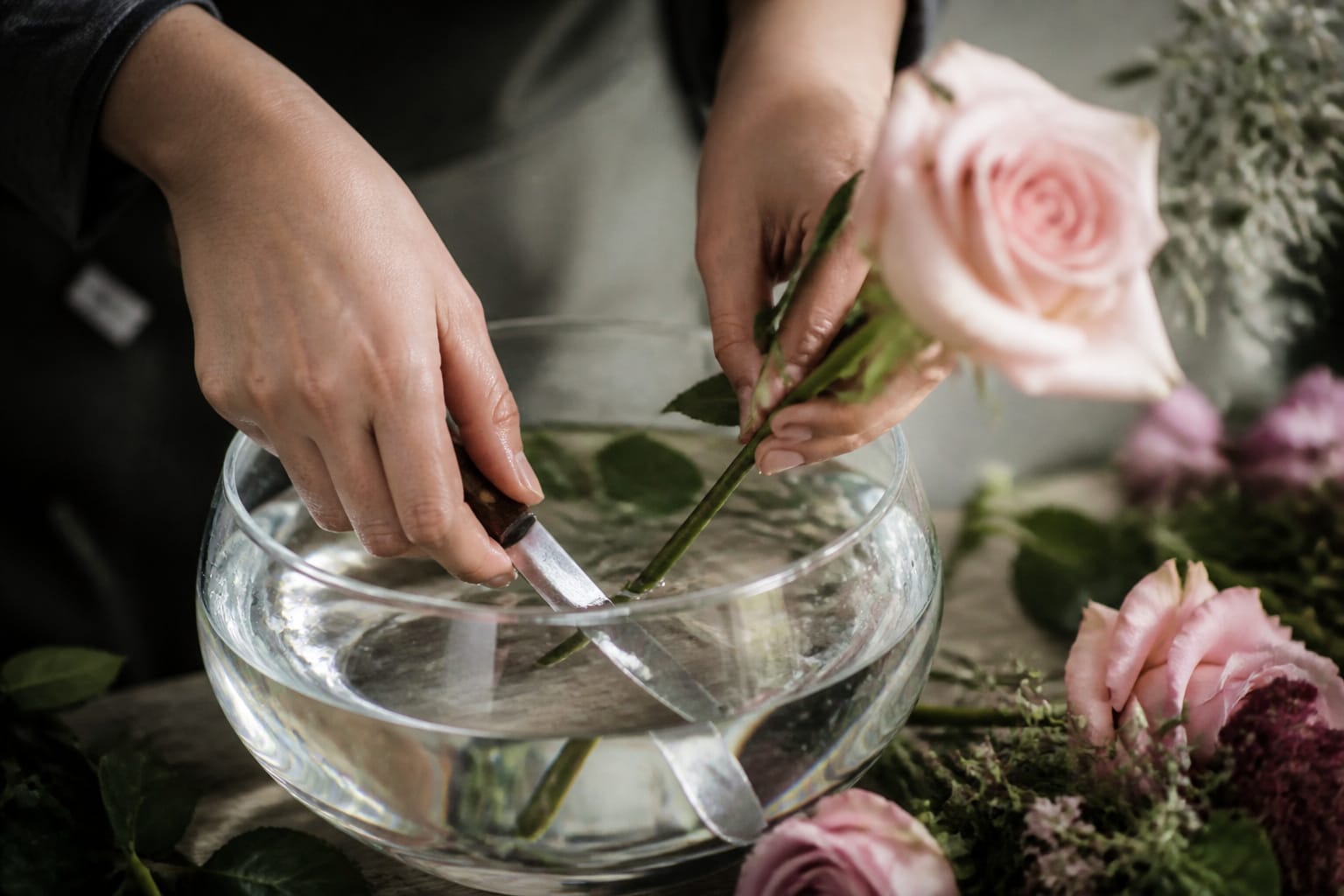 Florist cutting a rose stem underwater at an angle