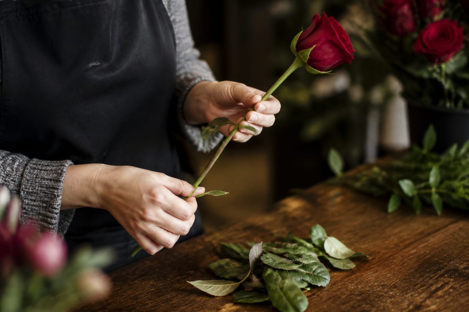 Florist stripping lower leaves from a rose stem before conditioning