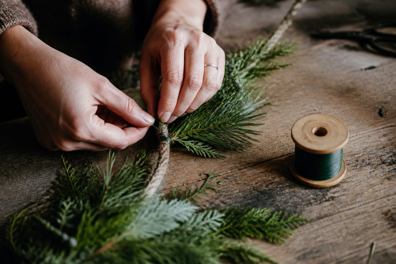 Hands wiring a small bundle of evergreen clippings onto a rope to build a garland