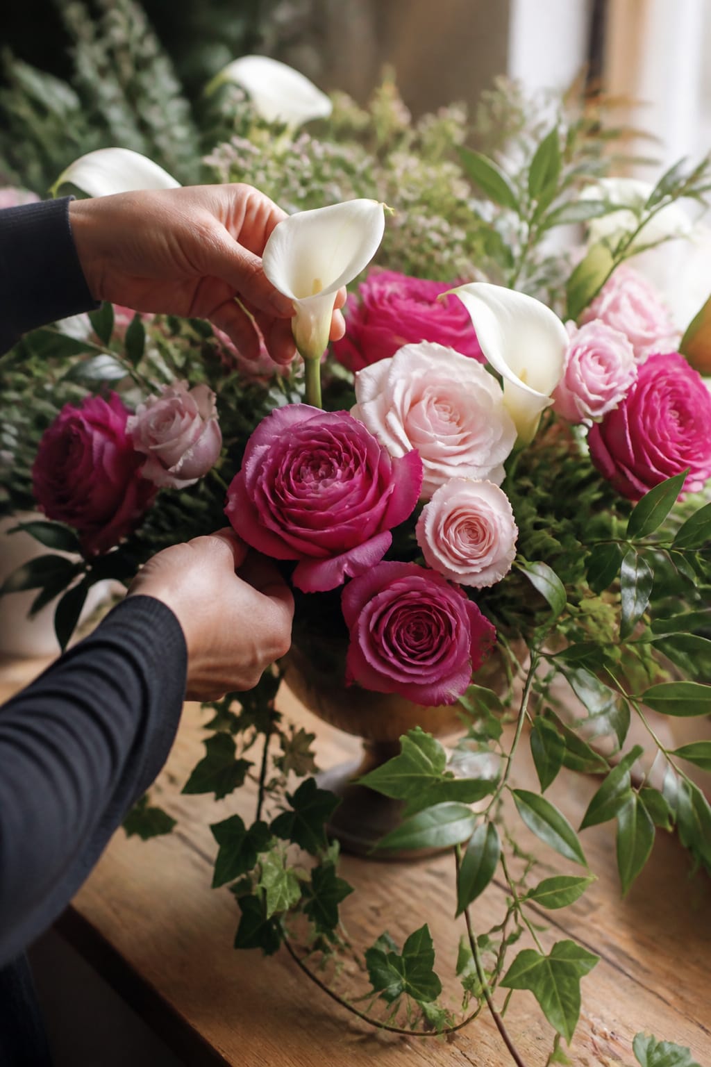 Calla lilies and foliage being added between roses in a front-facing arrangement