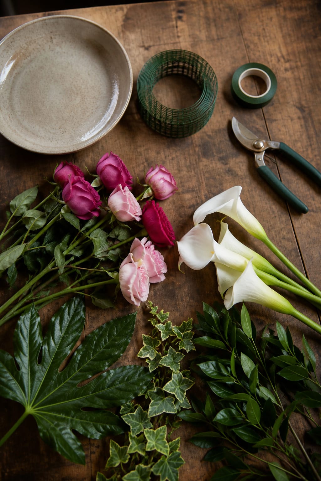 Florist worktable with wire mesh, roses, calla lilies, and foliage laid out