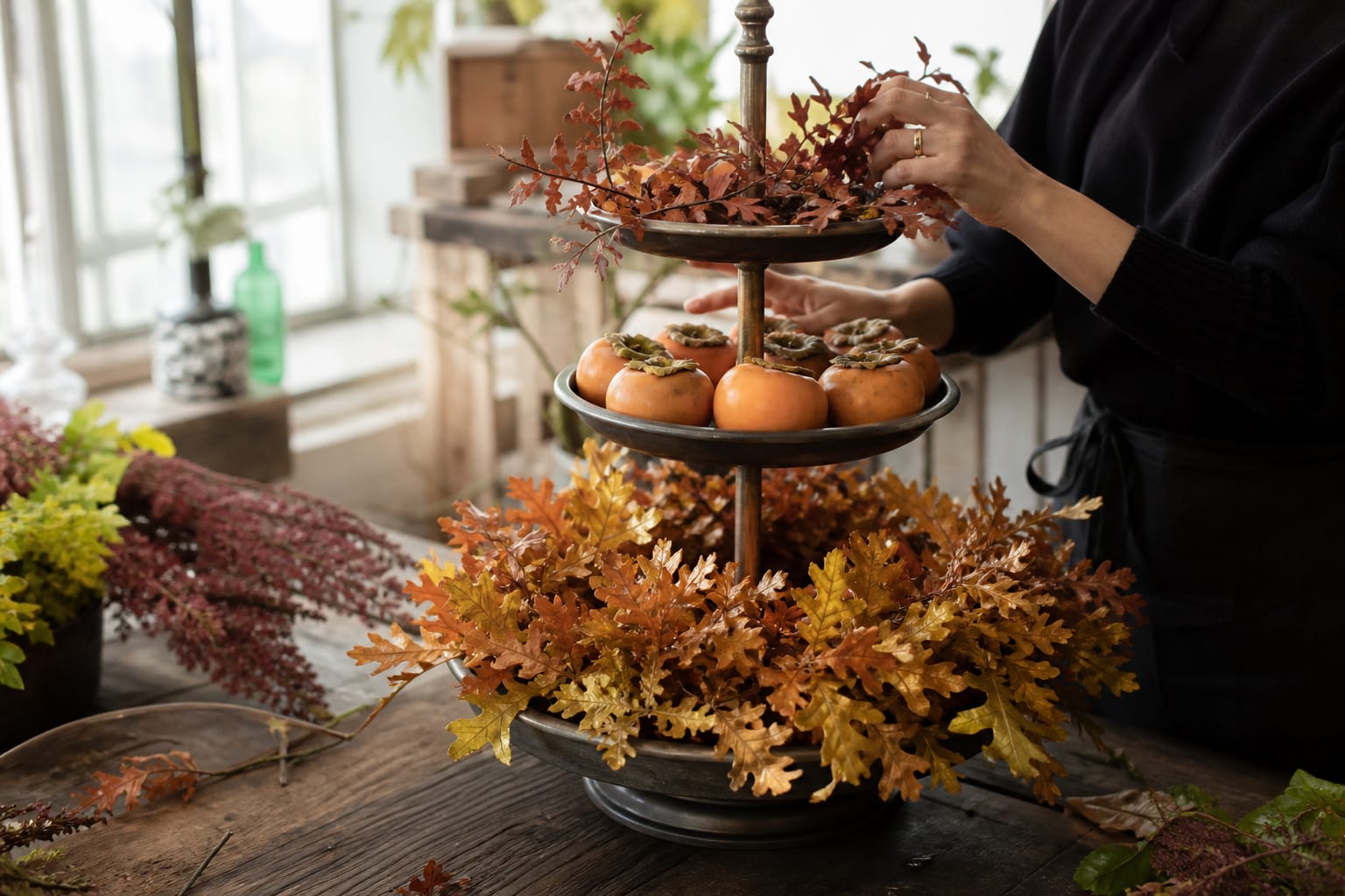 Three-tier dessert stand centerpiece layered with preserved foliage and persimmons