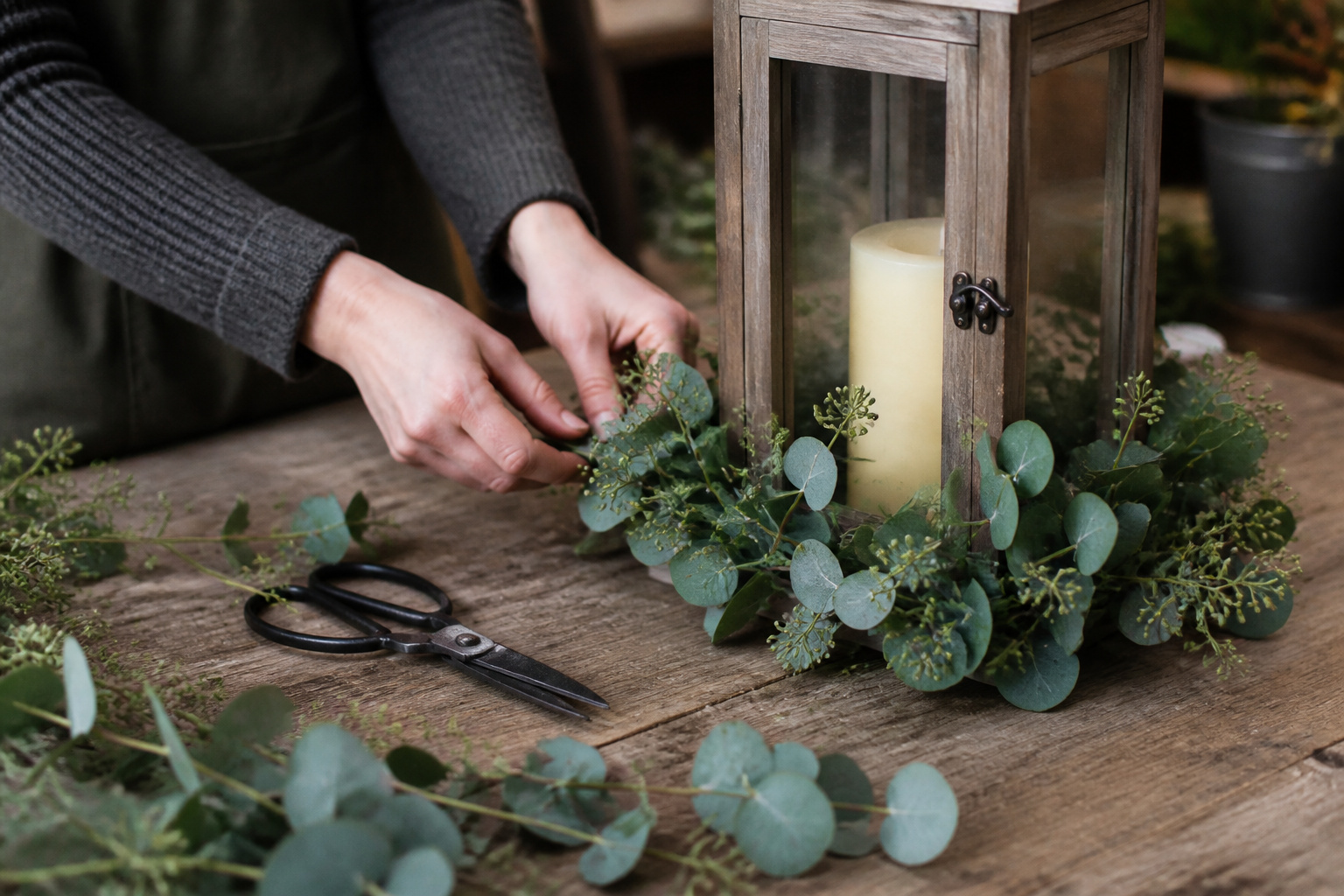 Fresh eucalyptus sprigs tucked around the base of a wooden lantern on a florist's worktable