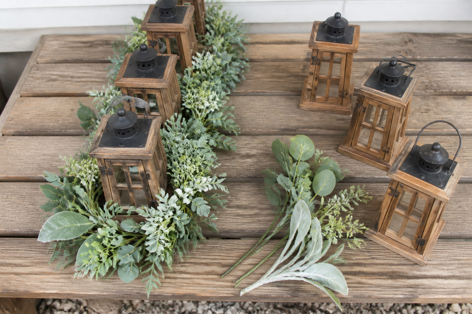 Matching lantern set and greenery beside loose individual lanterns and stems on a wooden bench