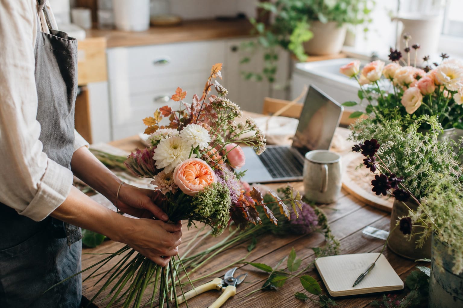 Florist arranging fresh flowers at a wooden worktable in a bright home studio