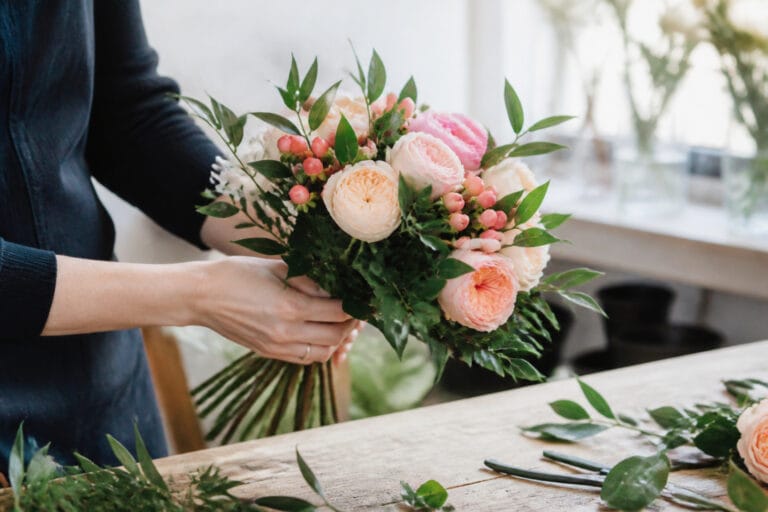 Florist's hands building a spiral hand-tied bouquet of garden roses and greenery