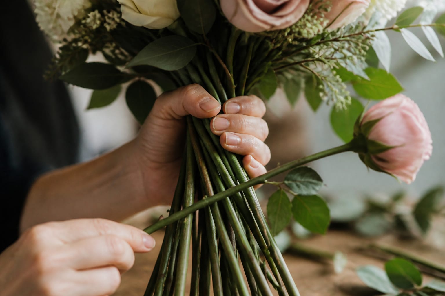 Hands adding a rose stem at an angle to build a spiral hand-tied bouquet