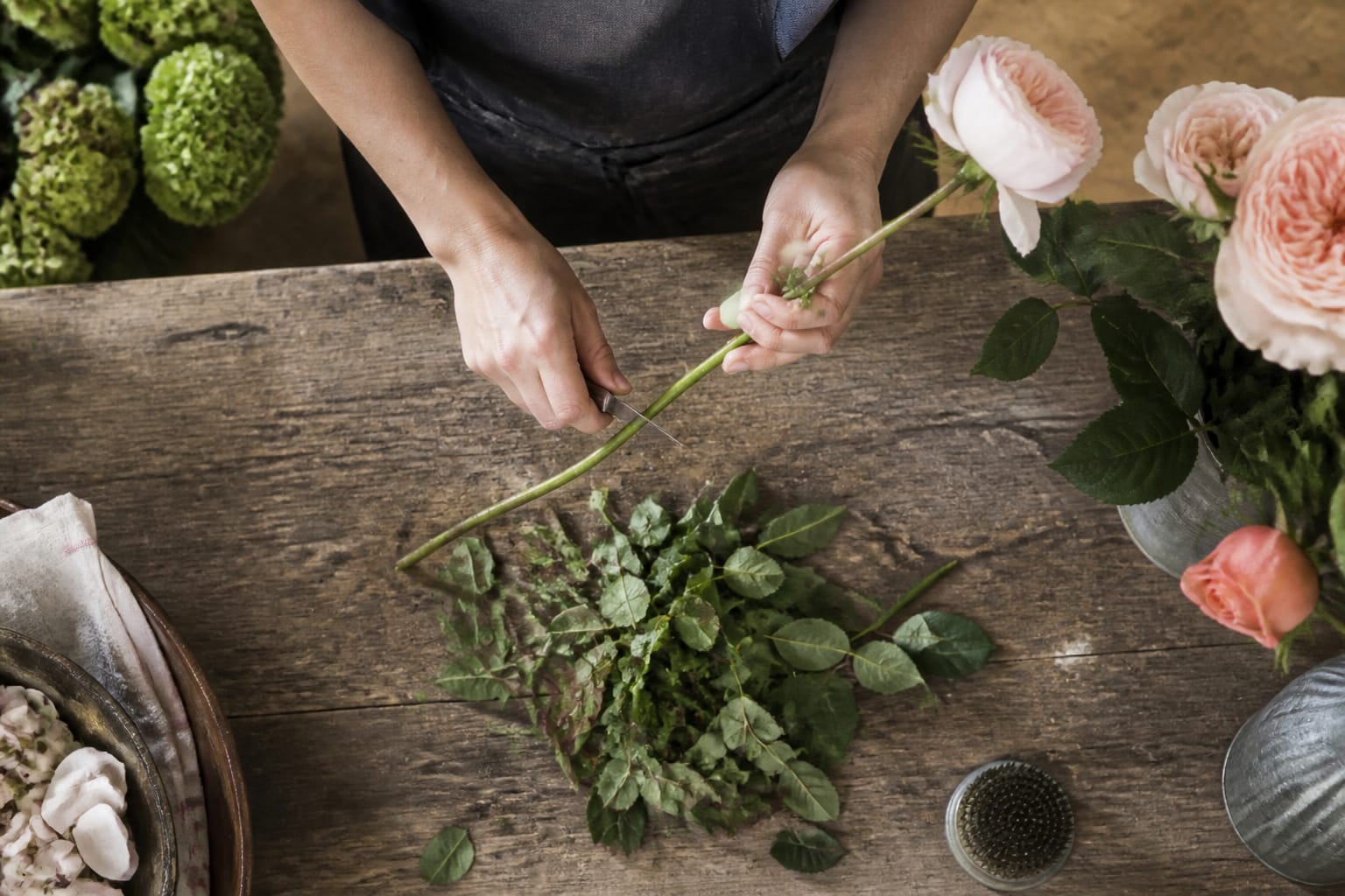 Florist stripping thorns and foliage from a rose stem with a floral knife