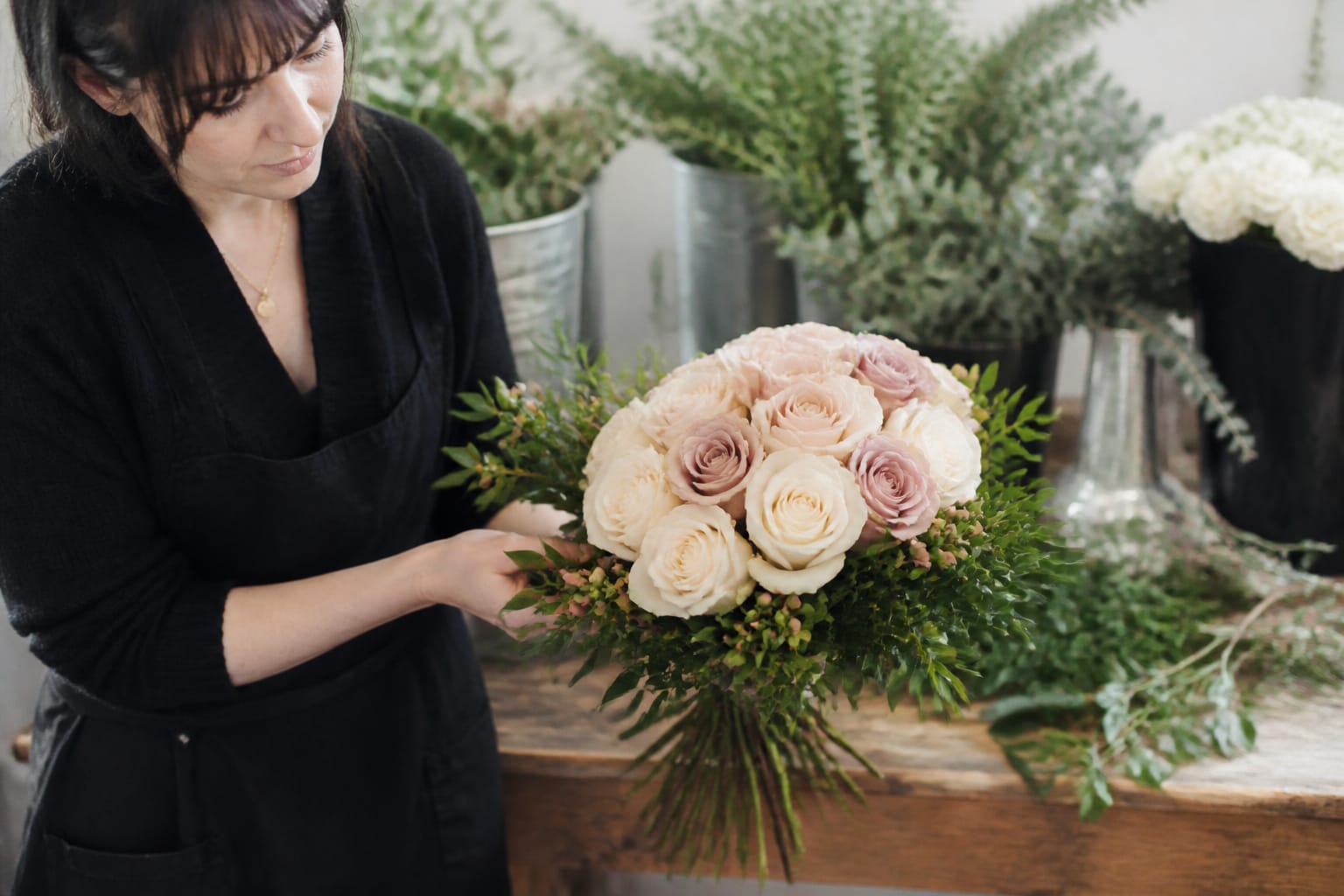 Florist adding ruscus and hypericum berries to a spiral rose bouquet